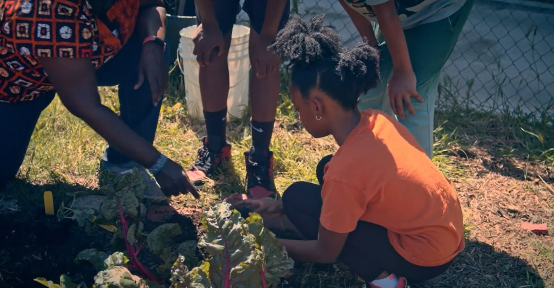 WEA Program Lead Rasheeda Hawk helping a young girl to plant at the Seeds of Carver gardens in LA. Credit: Women’s Earth Alliance/ Seeds of Carver